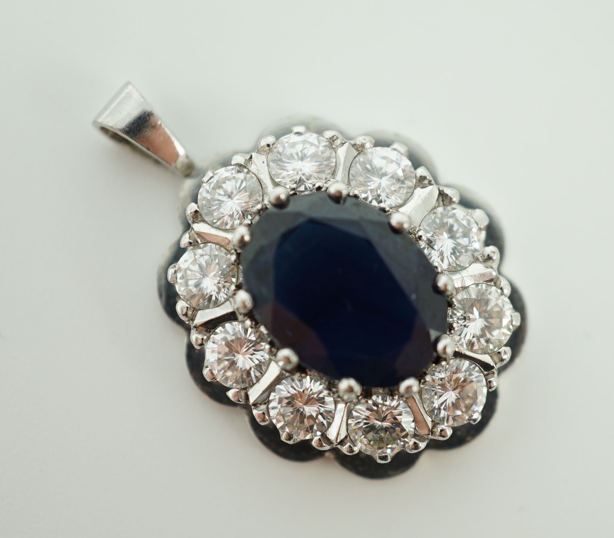 A modern 18ct white gold, sapphire and diamond set oval cluster pendant